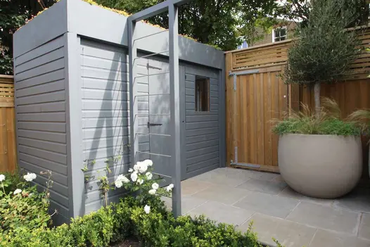 Small rectangular area paved with Heath sawn sandstone slabs next to tall fence with wooden security gate. Grey shed to left.