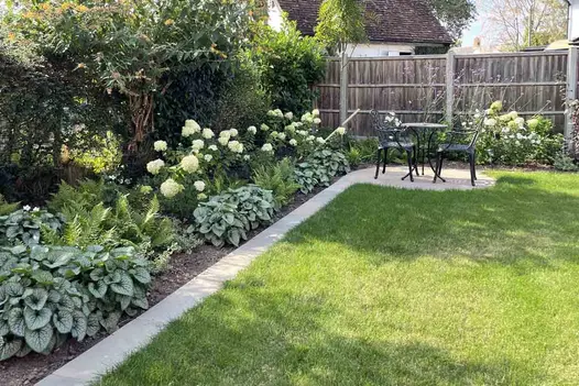 Bistro set on small round patio in corner of lawn with Raj Breen sandstone coping as mowing strip. Built by JG Landscaping