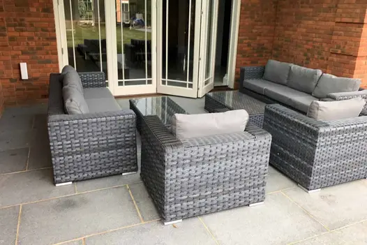 Cream folding doors partially open onto Flamed Grey sawn sandstone paving with rattan lounge set. Built by Ilife Developments.