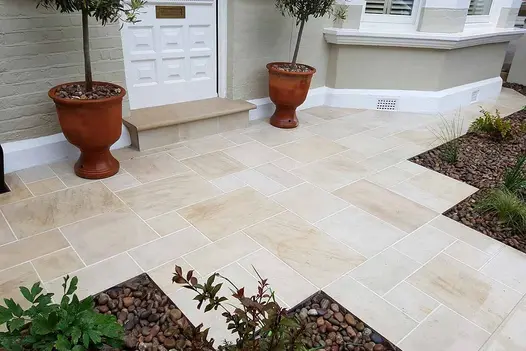 Path of Multi Mint sawn paving slabs with pale joints leads to wide paved area with step up to front door of bay-windowed house.