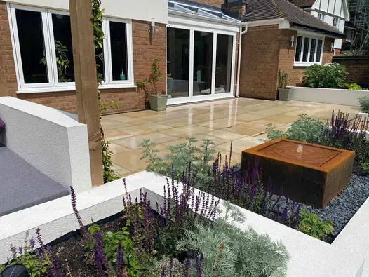 Patio of Light Buff sawn sandstone with square Corten steel water feature and white rendered raised beds at back of house.