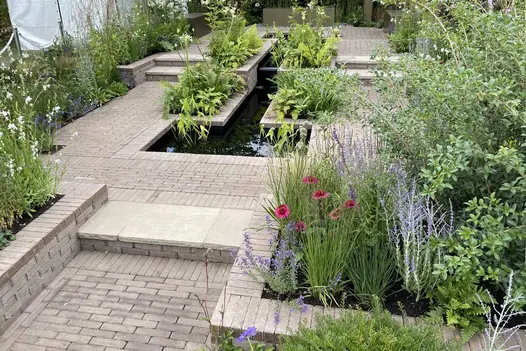 Stepped raised bed of Aldridge clay pavers with ferns and tall planting in Macmillan legacy RHS show garden built by Agents Green.