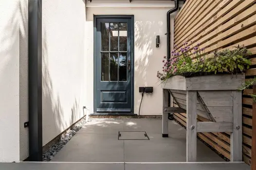 Small courtyard paved in Sidewalk porcelain leading to a modern front door of white rendered house.
