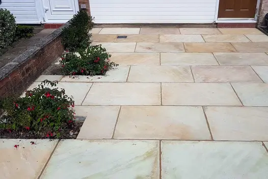 2 fuchsias planted in pits next to low wall in front garden fully paved with mint Indian sandstone slaps laid running bond.