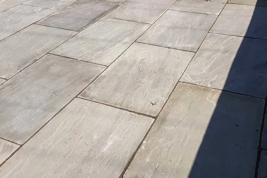 Close view of Kandla Grey Indian sandstone paving laid running bond with dark pointing, showing riven surface. 