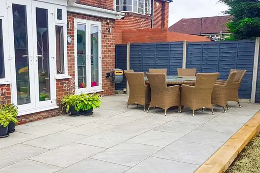 Round rattan dining set on Kandla Grey Indian sandstone paving with wooden sleeper edging in front of 2 sets of french doors.