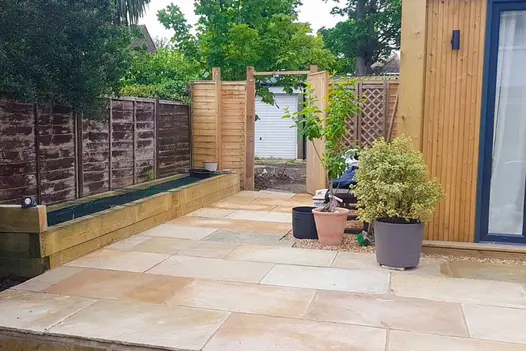 Corner of Mint Indian sandstone patio and side return edged with pots and wooden sleeper raised bed. Design by Silva Tree.