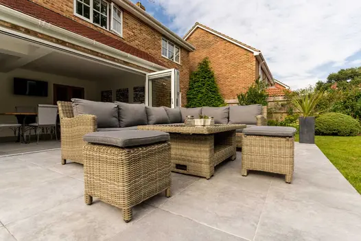 8-seater rattan lounge set on patio of Silver Contro Porcelain outdoor pavers, with open bifold doors into rear of suburban house.