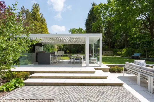 Area of Silver Grey Multi clay pavers leads to wide steps up to patio under large louvred pergola. Design by Barnes Walker.