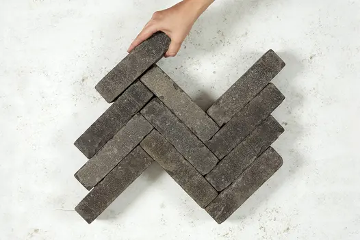 Hand adds 11th brick to 10 Silver Grey Multi brick pavers in 3 zigzag rows on light background. Free UK delivery available.