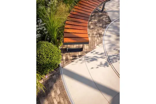 Near view of edge of paved stone circle with Stone Grey clay paver insert under curved wooden bench. Design by Lynn Cordall.