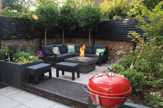 Silver Grey porcelain paves area with corner sofa and firepit table. Step and low riser of Charcoal Grey clay pavers in foreground.