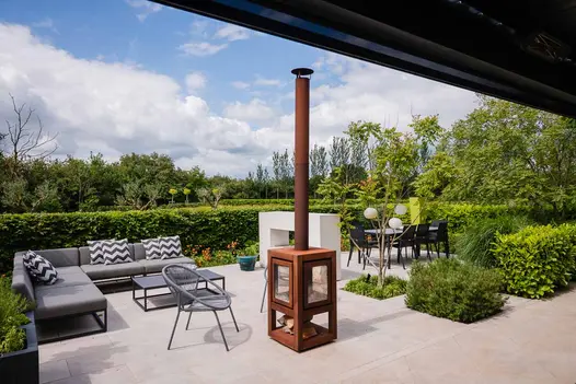 Outdoor lounge and dining area in secluded garden covered by bushes with Silver Grey Porcelain paving and firepit.