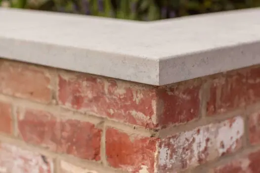 Close view of corner of 2 brick walls meeting, topped with Jura grey limestone coping. Design by Simon Orchard.