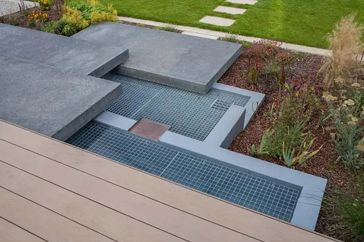Contemporary garden shows mocha designboard decking lead down chunky steps combined with water feature.