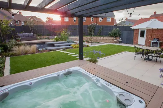 Sun shines through wooden pergola with hottub bubbling underneath, surrounded by mocha designboard composite decking.