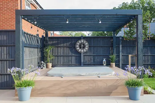 Wooden pergola stands over covered hot tub with mocha designboard composite decking surrounding the tub.