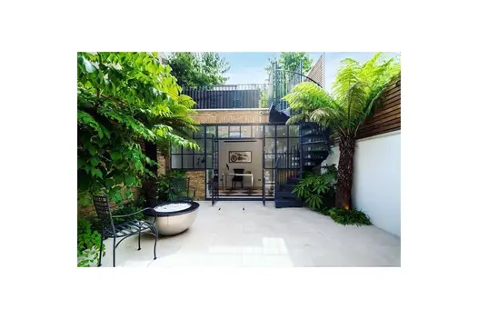 Slab Khaki Porcelain used in enclosed patio, a palm tree sits next to a spiral staircase next to impressive glass doors.
