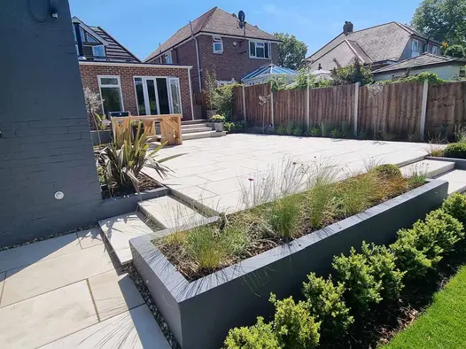 3 shallow steps up to large rectangular patio of Beige smooth paving slabs, with steps up to house extension on far side.