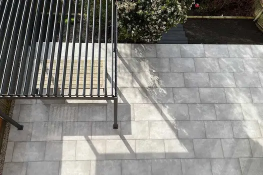 Venetian Grey Porcelain paved patio with a metal pergola and seating area in the left corner.