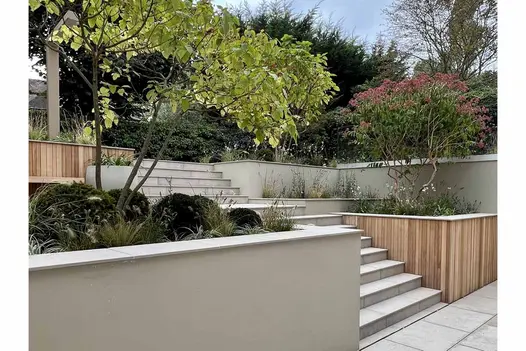 On steep slope, from paved area, steps rise between terraced beds topped with Jura Grey coping with 5mm chamfer edge.