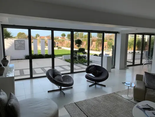 View through wide bifold doors from inside monochrome room to huge modern garden with lawn and Harvest sawn sandstone paving.