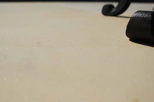 Close-up of Harvest smooth sandstone slabs, showing beige tones, with curled base of 2 metal chair legs to right.