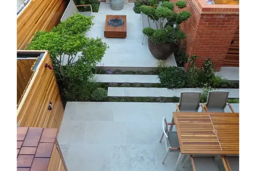 View down onto narrow garden with small multi-stemmed trees. Completely paved on 2 levels with Jura Grey sawn limestone slabs.
