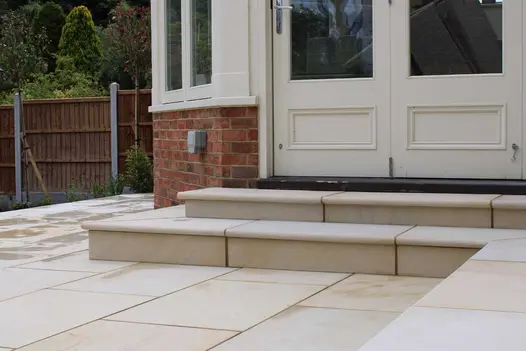 2 bullnose Harvest sawn sandstone steps rise to wooden folding doors from patio in matching paving by Essex Garden Design.