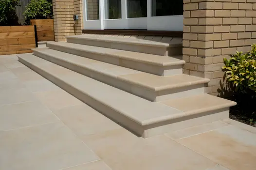 4 harvest sawn sandstone bullnose steps lead up to white french doors against light brick house, away from matching sandstone patio.