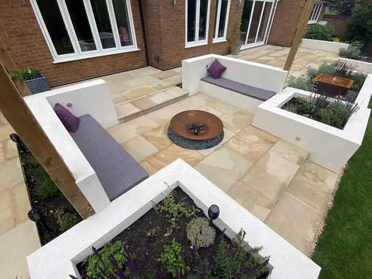 View down onto 2 raised beds with attached benches either side of metal fire bowl on large Light Buff sawn sandstone patio.
