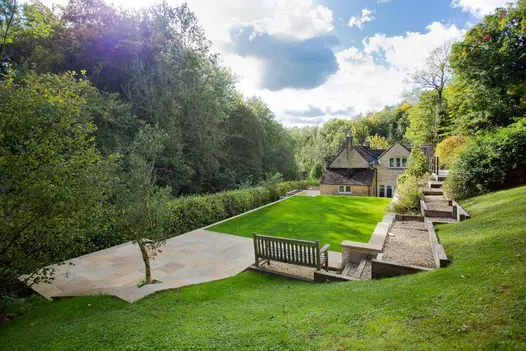 Camel Dust sandstone patio at far end of large grassed garden from rural cottage. Gravel stepped path rises to viewing platform.