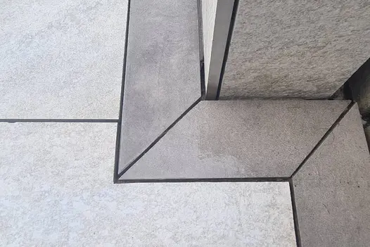 Close up corner shot of light coloured porcelain paving and Steel Grey Porcelain Planks, used as a border.
