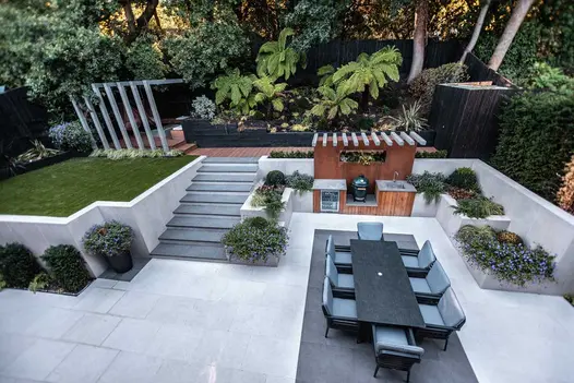 Steel Grey porcelain steps with white flanking walls rise from light paving to deck and lawn area. Design by Gardens of the Future.