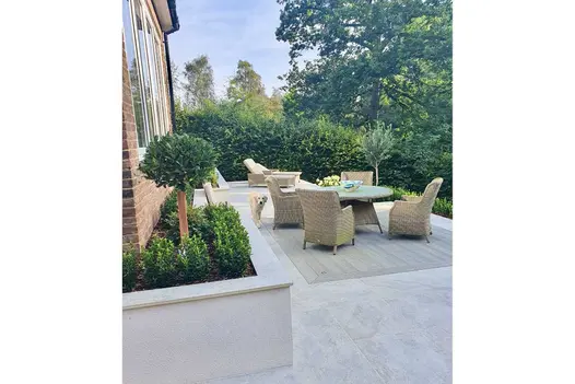 Dog by luxury rattan furniture on composite decking set into Steel Grey Porcelain Paving on patio terrace with raised beds.