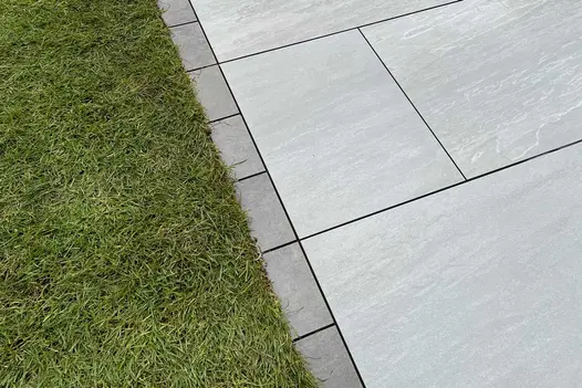 Close view of Steel Grey porcelain setts with dark grouting creating edge between pale paving and lawn. Built by Green Life.