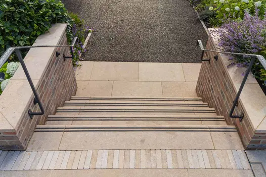 Wide steps with acid washed limestone and black grip insets, leading to a gravel garden path with planting.