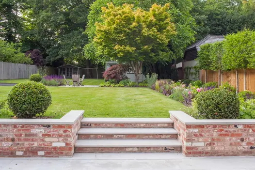 3 Jura Grey limestone bullnose steps rise between flanking brick walls from matching patio to lawn. Design by Simon Orchard.