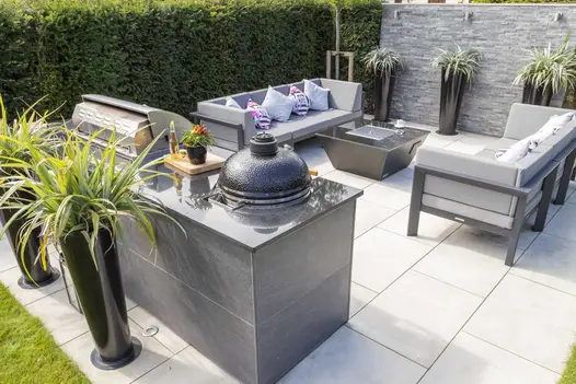 Outdoor kitchen forms edge of patio with 2 sofas and fire pit, opposite high wall with Green Slate cladding. Design by Cube 1994.