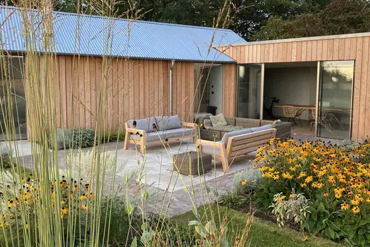 Wide strip of Stone Grey clay pavers frames sawn limestone patio between herbaceous border and wood-clad building.