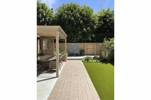 At back of house Stone Grey Clay Pavers lead to water feature and separate paved patio with pergola-covered dining area from lawn.