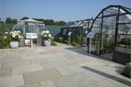 5 steps with white risers rise from Kota Brown limestone paving edged with planting to deck area with wooden dining set.