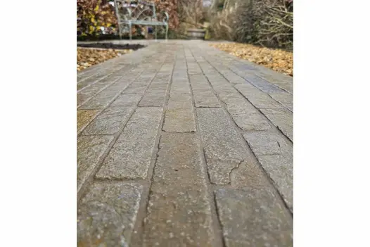 Close-up of Antique Yellow Stone Pavers forming a path down an alleyway, bordered by pebbles on either side, leading to a metal bench.
