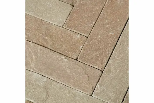 Close view of Raj Green tumbled sandstone pavers, laid herringbone, without mortar, showing riven surface and colour tones.