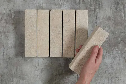 5 Egyptian Beige stone pavers laid in row on grey background. A hand is placing a 6th brick at an angle on top.