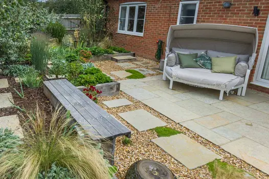 Rear garden paved with gravel and Antique Yellow limestone patio slabs, with mulched soil, wooden bench and sleeper-built beds.