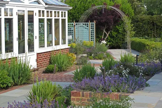 Kota Brown stone  paving and clay pavers laid on 2 levels outside conservatory, with clipped hedging, lavender and a rose arch.