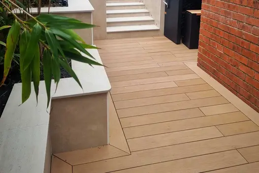 Mocha DesignBoard composite decking between brick wall and raised bed faced with porcelain. Design by Stonecraft of Lancashire.