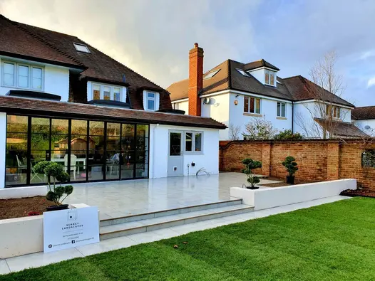 Large raised garden terrace paved with Light Grey Porcelain coming straight off large patio doors and stepping down onto a large lawn.