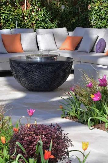 Jura Beige sawn limestone path between beds planted with pink and orange tulips leads to patio with outdoor furniture.